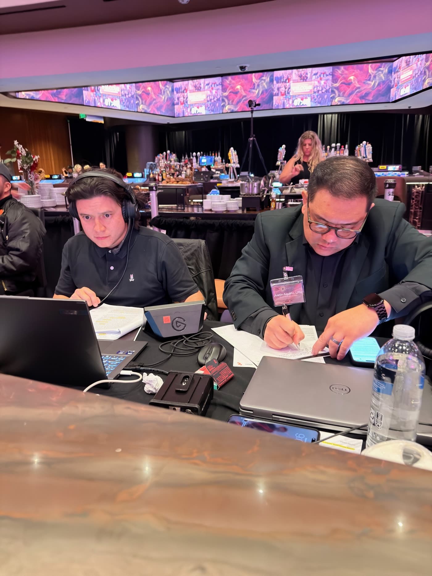 Two operators on headsets at the booth, laptops open, mid show