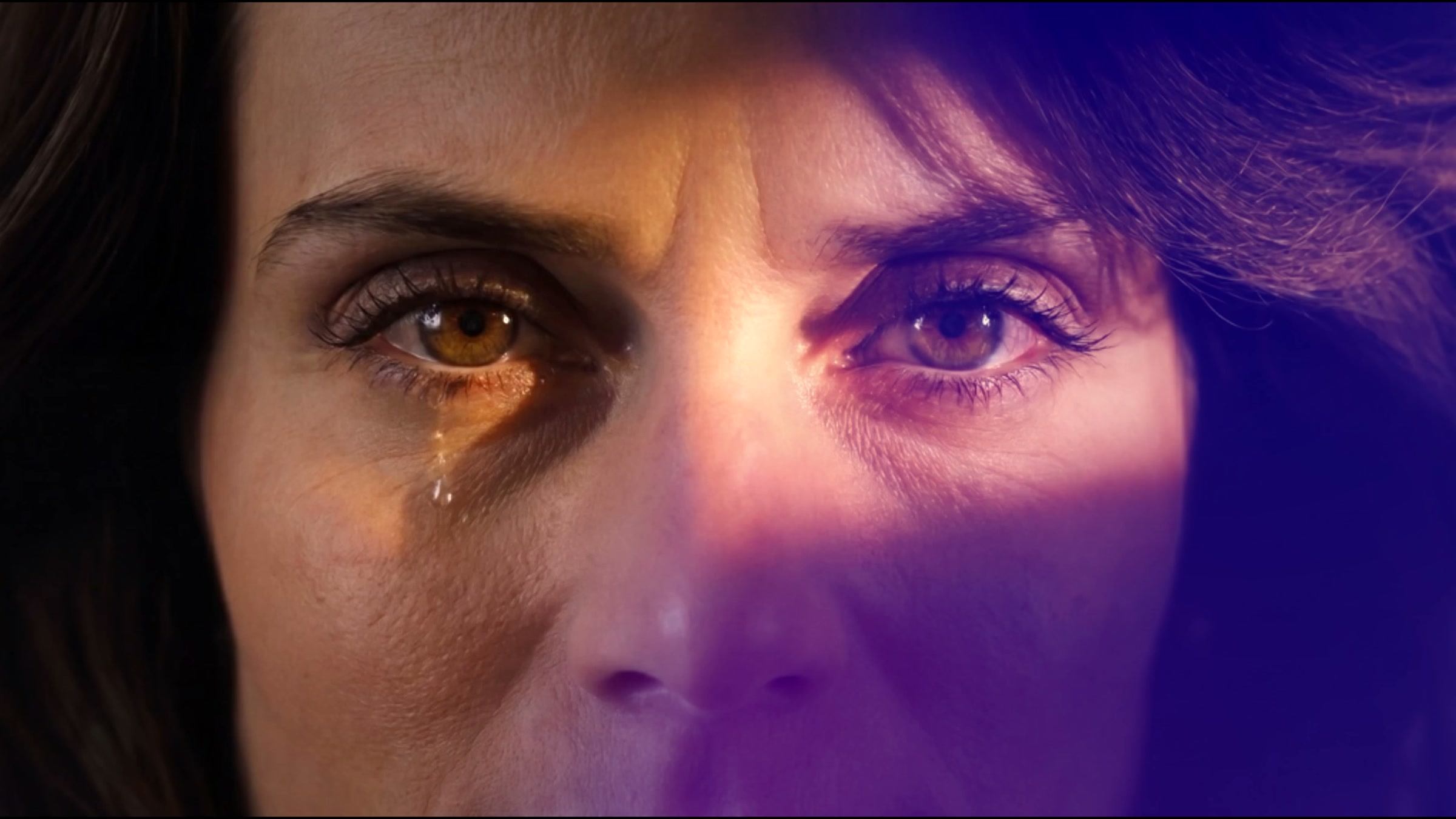 Film still, a face lit violet on one side and gold on the other