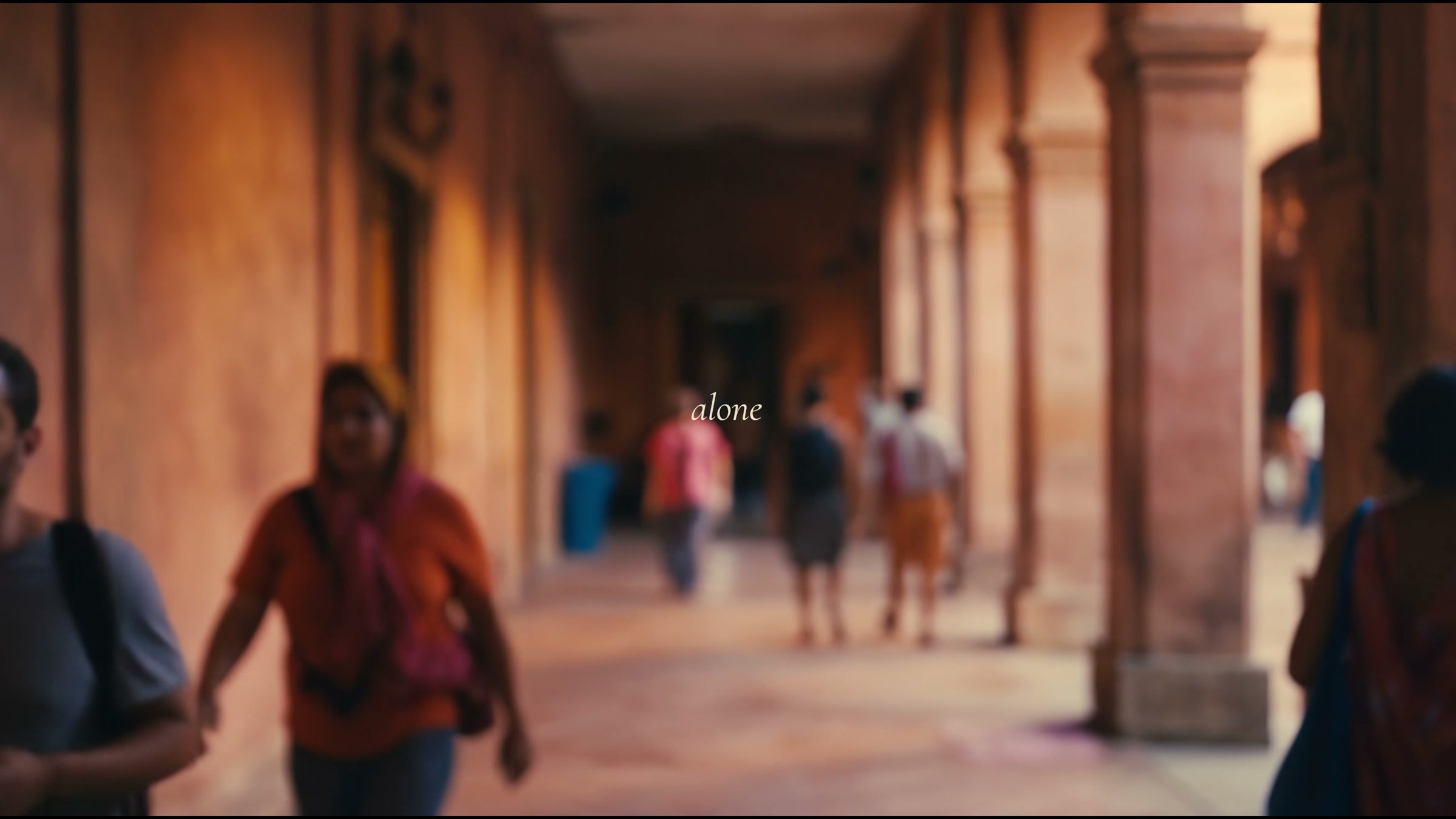 Film still, a corridor of people passing a figure standing still